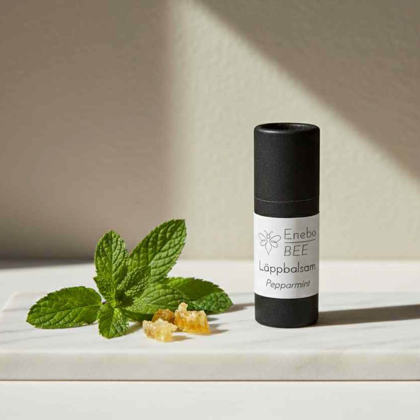 EneboBee läppbalsam Pepparmint i papptub tillsammans med färsk mynta och bivax.