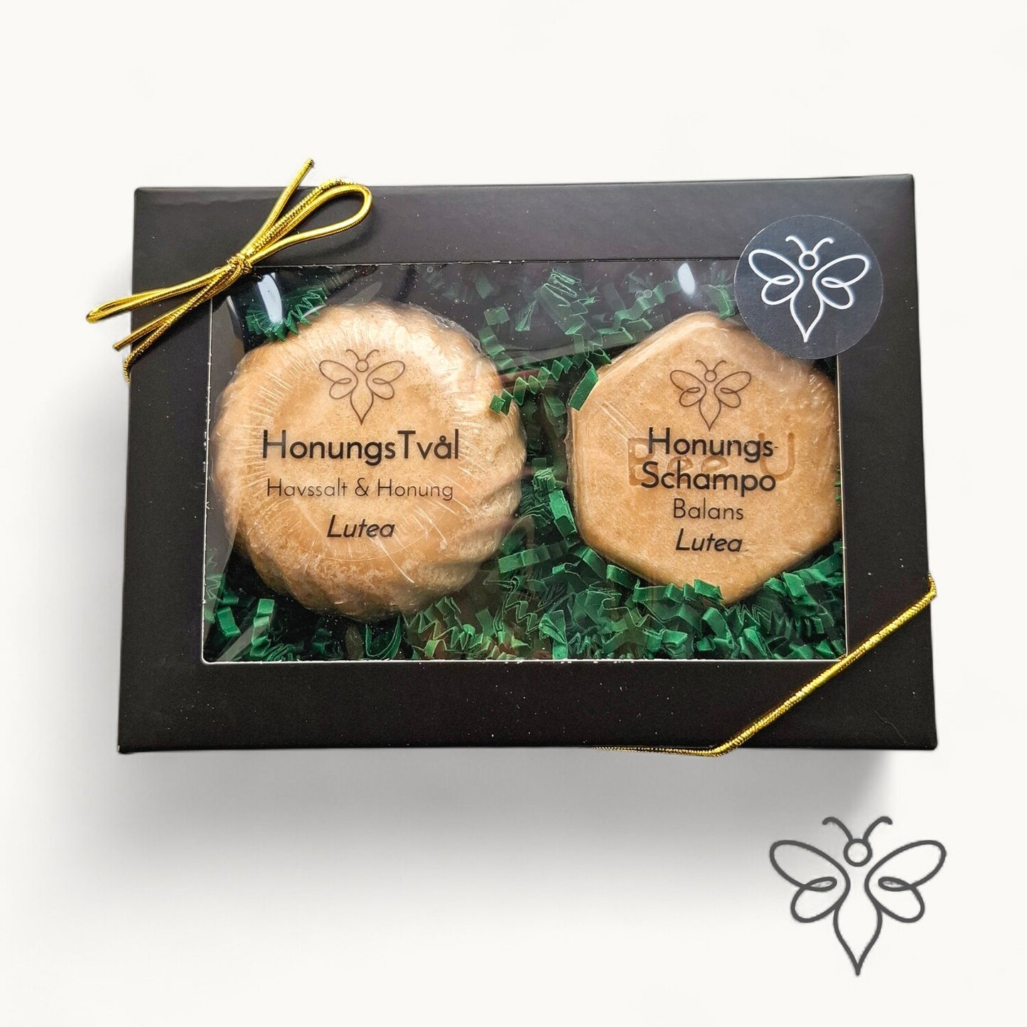 Stängd presentask, Lutea, med honungstvål och schampokaka från EneoBee, svart ask med fönster och guldsnöre.