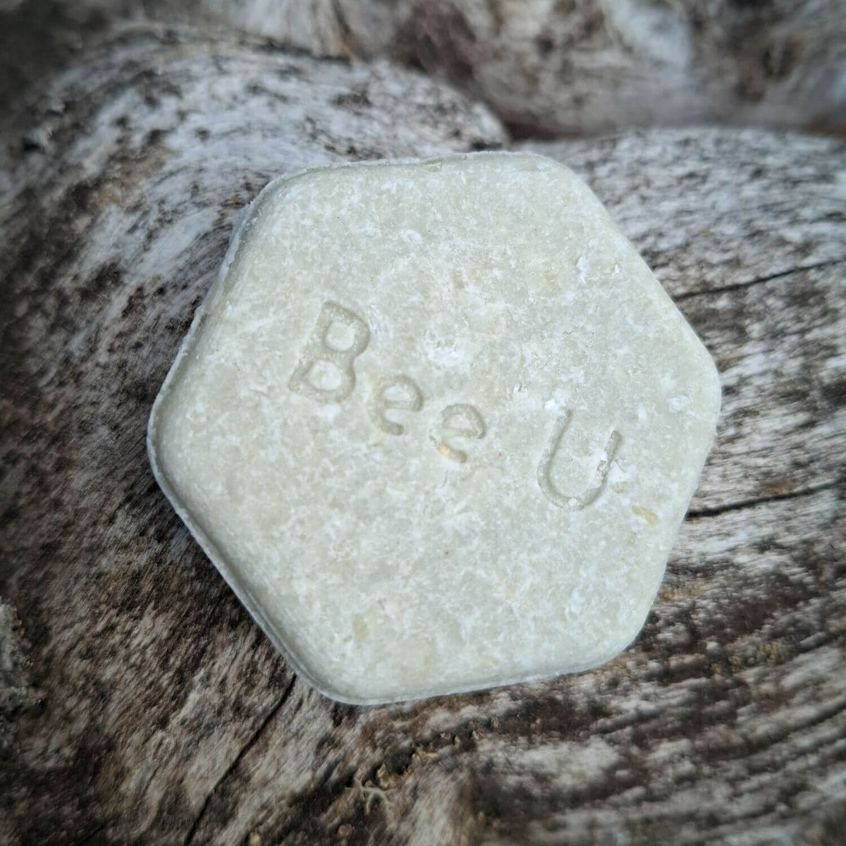 EneboBee schampokaka med honung, ljust olivgrön med hexagonform mot grånat trä.