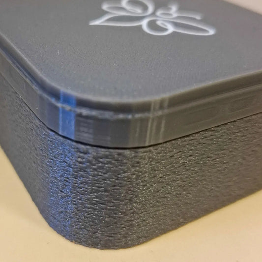 Grå 3D-printad ask för balsamkaka med vit logotyp. Exemplar från Avskedshyllan till reducerat pris.