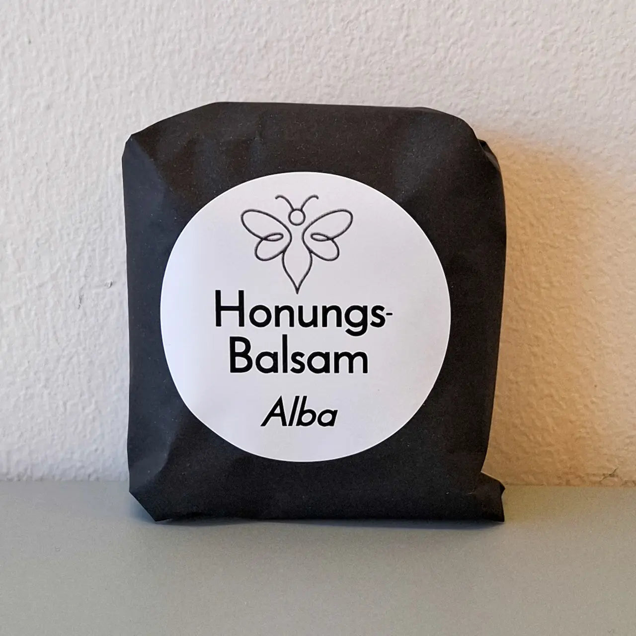 EneboBee handgjord balsamkaka 'HonungsBalsam Alba' förpackad i svart papper med vit rund etikett.