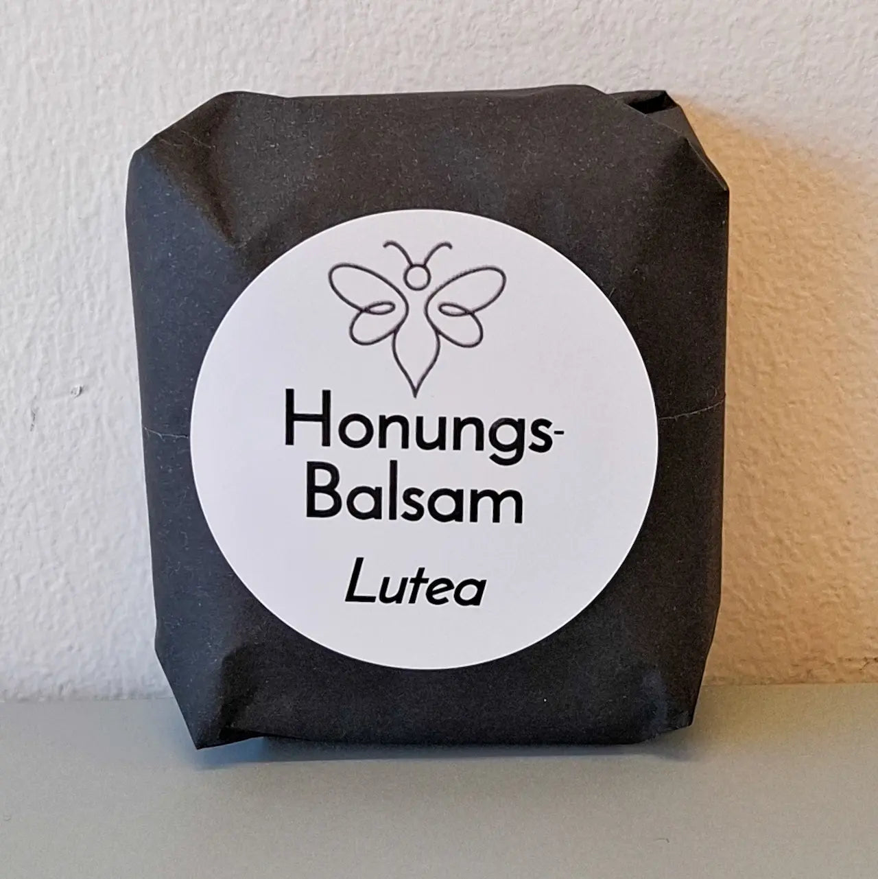 EneboBee handgjord balsamkaka 'HonungsBalsam Lutea' förpackad i svart papper med vit rund etikett.