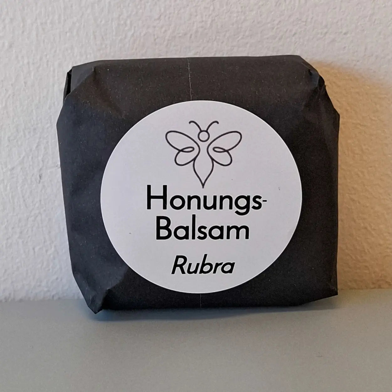 EneboBee handgjord balsamkaka 'HonungsBalsam Rubra' förpackad i svart papper med vit rund etikett.