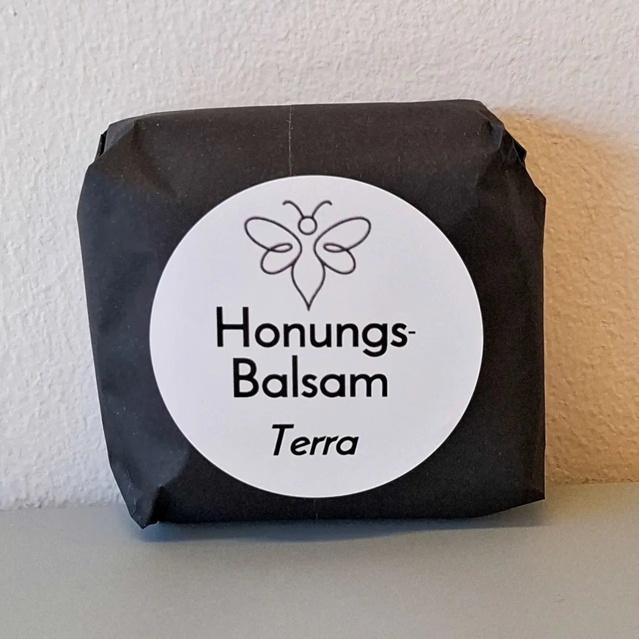 EneboBee handgjord balsamkaka 'HonungsBalsam Terra' förpackad i svart papper med vit rund etikett.