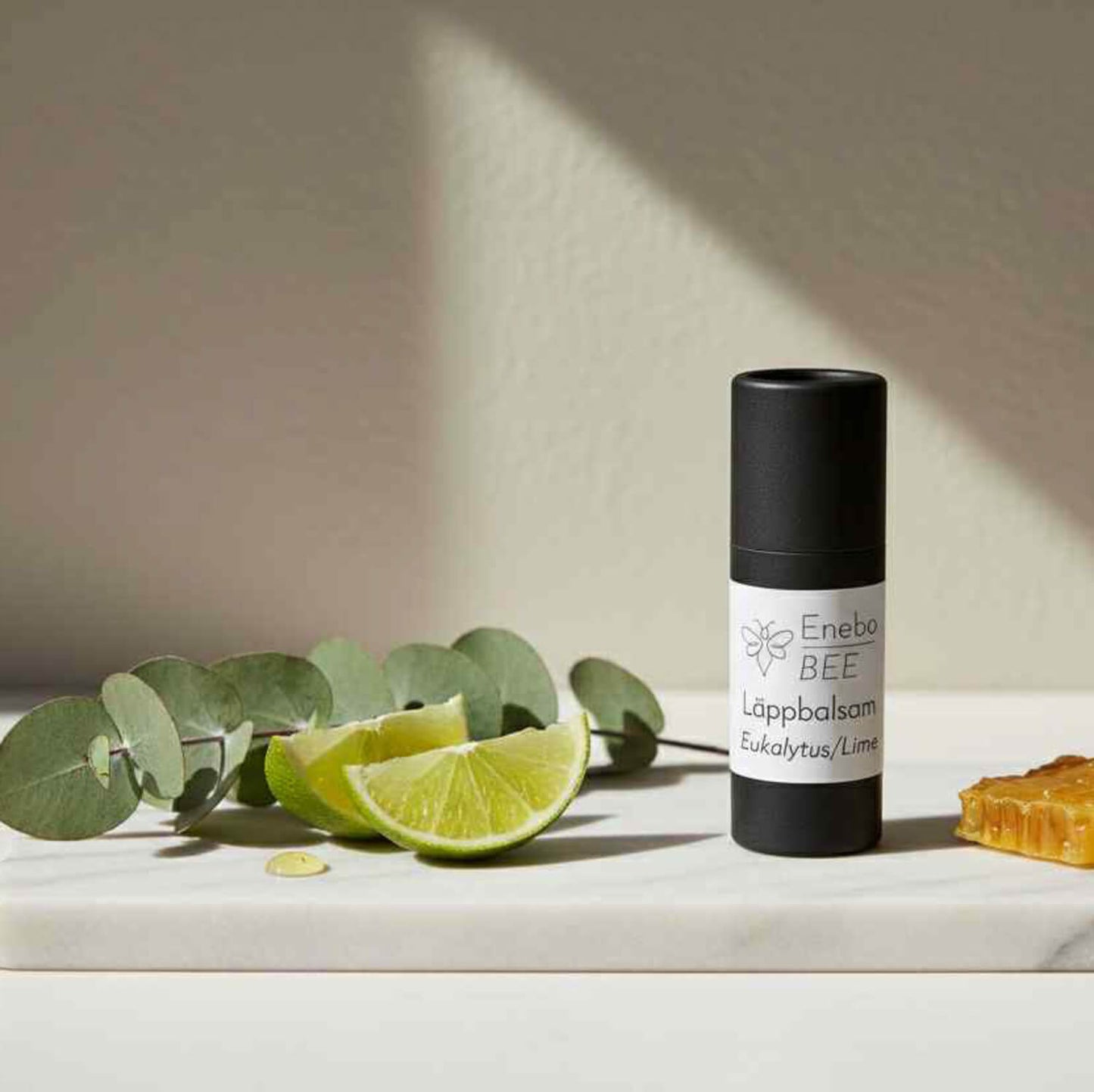 EneboBee läppbalsam Eukalyptus & Lime i papptub med eukalyptusblad, limeklyftor och honung i bivaxkaka.