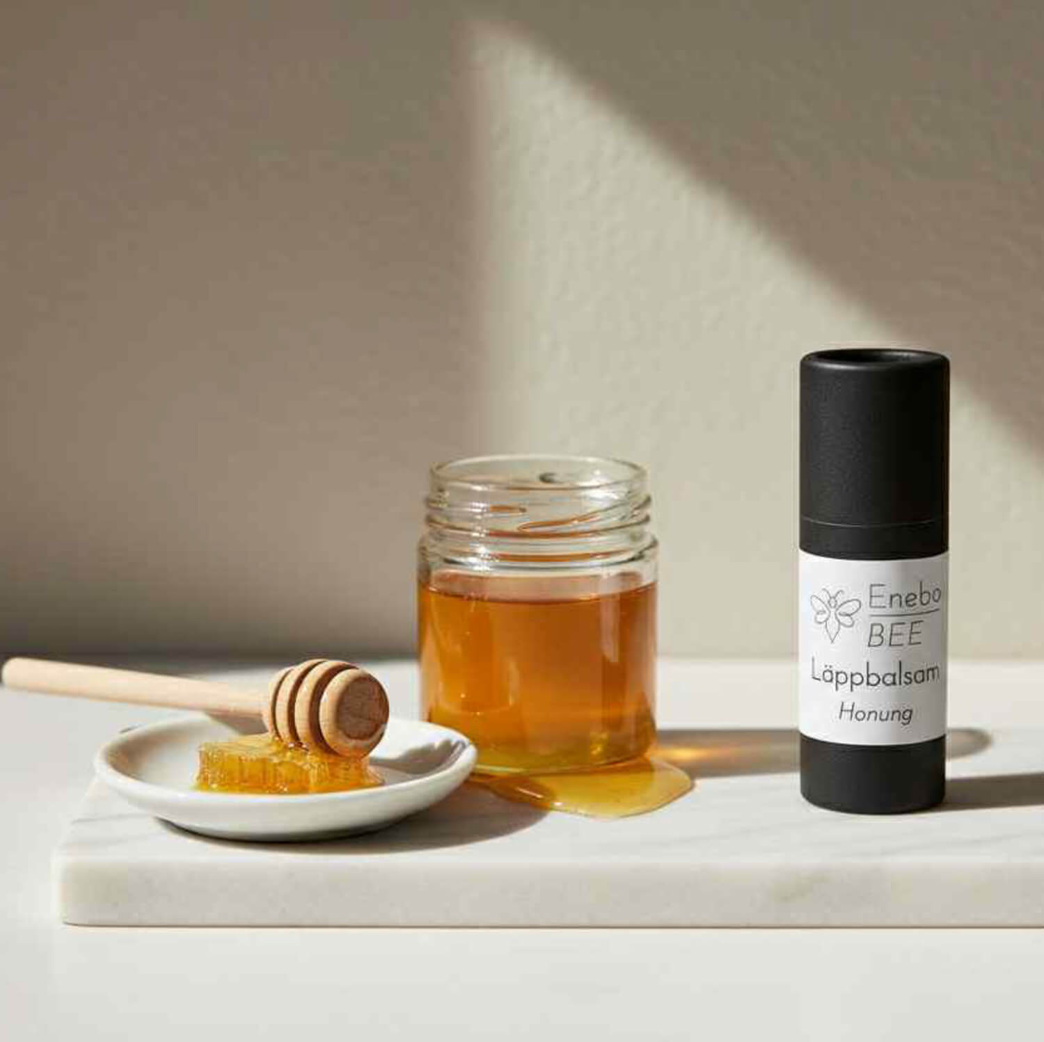 EneboBee läppbalsam Honung i papptub tillsammans med honung och honungssked.